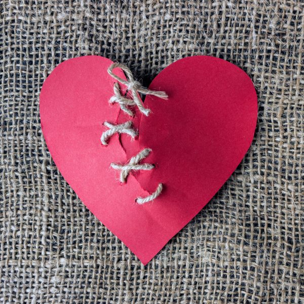 A broken red heart. Sewn thread. The concept of divorce, separation, quarrel.